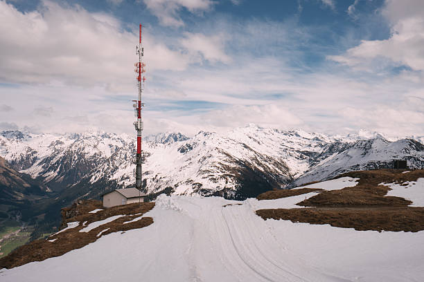 Red and white telecommunication tower and small building standing on a snowy mountain peak, with a breathtaking view of the surrounding alpine landscape