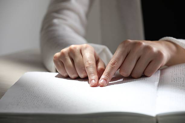 istock Blind woman reading book written in Braille at table, closeup 2216799962