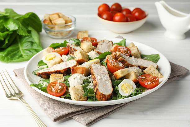 istock Tasty Caesar salad with chicken and tomatoes on white wooden table 2216804000