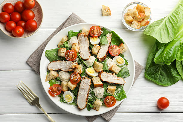 istock Tasty Caesar salad with chicken and tomatoes on white wooden table, flat lay 2216804007