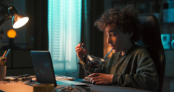 istock In a softly lit room, a child works on a robot, fixing cables and creating a toy computer system. He chats with a friend via webcam while soldering at his desk in the evening. 2216804027
