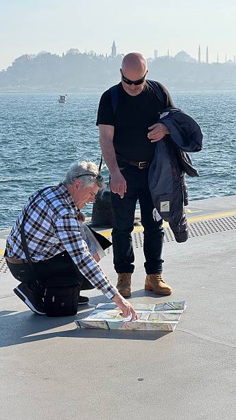Istanbul, Turkey — march 16, 2025: Two old mature travelers study map sunny pier. Tourist man points location, trip discussion. Adventure exploration. Curiosity spirit of travel. Tourism, explore new city, country.