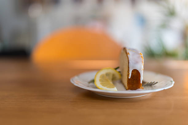 Slice of a lemon cake with lemon slice served on a white plate on wood table