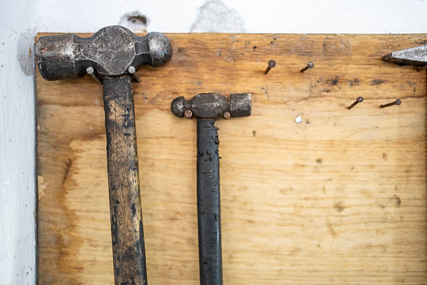 Two rustic hammers with worn handles are displayed alongside rusty nails on a wooden board, showcasing essential tools often used in carpentry and home projects.