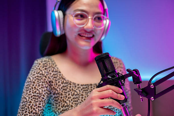 istock Content creator woman host streaming her a podcast with headphones and microphone interview cheering guest conversation broadcast studio with neon light. Blogger motivation recording voice over radio 2216824419