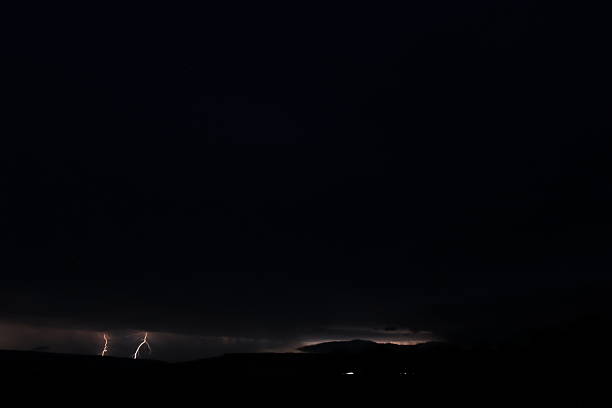 Bright flashes of lightning streak across the clouds, revealing a vibrant city beneath a stormy sky.