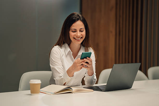istock Businesswoman smiling and using smartphone in office at night 2216827276
