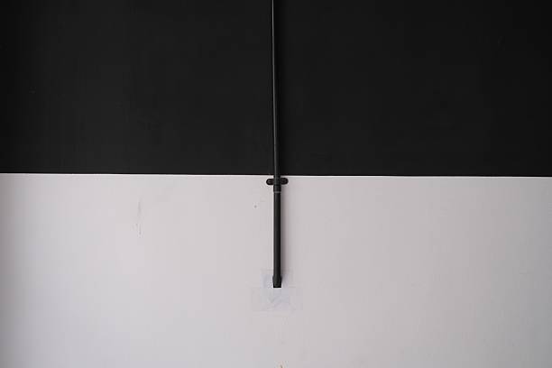 Minimalist interior wall design with a vertical black electrical conduit running down the center, dividing a stark black upper section from a clean white lower section.
