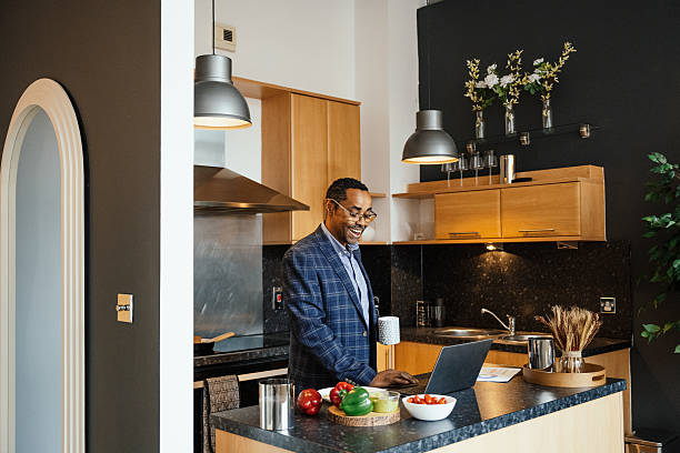 istock Black businessman in modern apartment and kitchen using laptop during breakfast, sipping cup of tea 2216836396