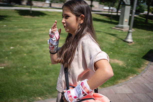 A young girl is enjoying outdoor activities on a sunny day, wearing protective wrist gear. She appears happy and is in an open park area with green grass and walking paths.