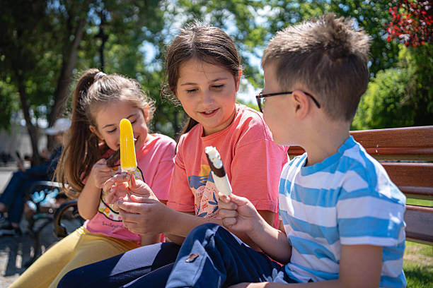 istock Three children enjoying ice cream together on a sunny park bench 2216837532
