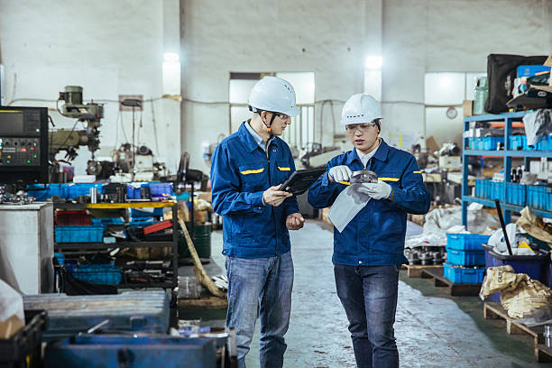 Two Asian workers holding tablet and blueprints in factory