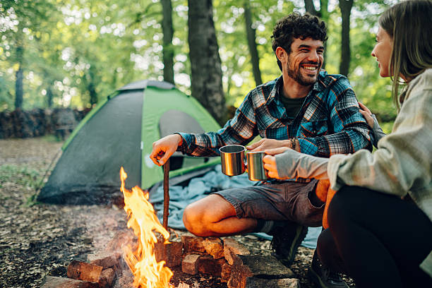 istock Happy campers drinking hot beverages around campfire in forest 2216843299