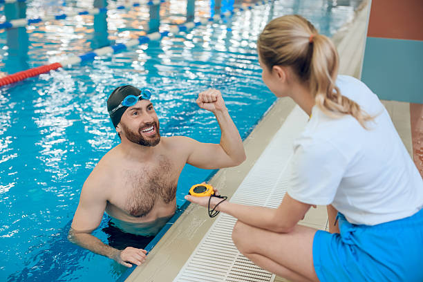 Close-up of swimming trainer using timekeeper while preparing junior league for completion in swimming pool