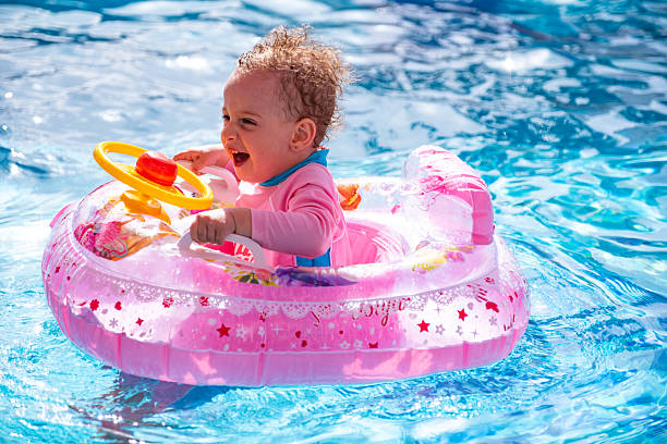 A cheerful child in a pink inflatable swim ring smiling brightly while playing in a blue pool. The warm sunlight enhances the joyful scene, symbolizing summer fun and delightful childhood moments.