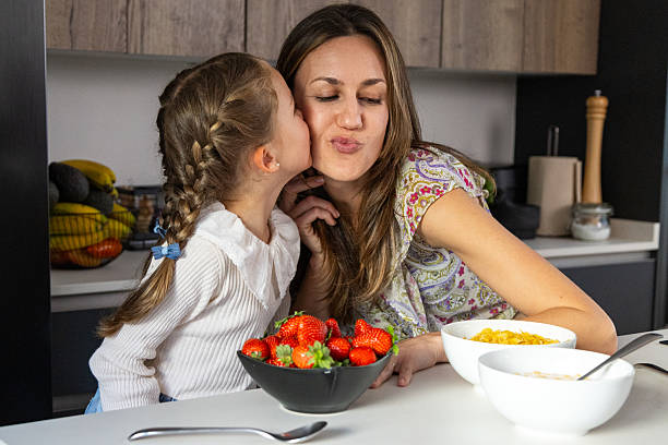 istock Daughter kissing mother while having breakfast in the kitchen 2216866932