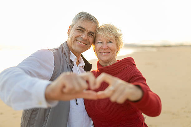 istock Happy senior couple making heart shape with hands on beach at sunset 2216869509
