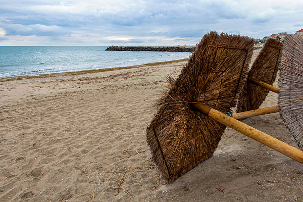 Empty off-season sandy beach with beach umbrellas on the ground under stormy sky at Pomorie, Province of Burgas, Bulgarian Black Sea coast