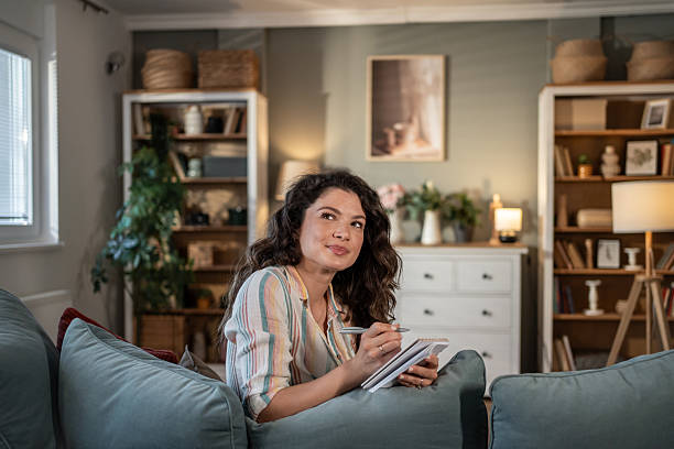 istock Young woman taking notes on sofa and thinking in living room 2216885713