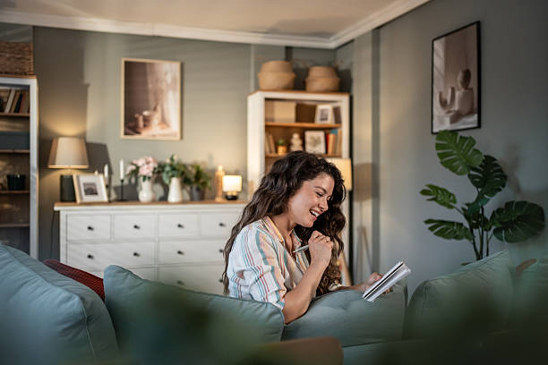 Young woman lying on sofa and writing in notebook, having fun