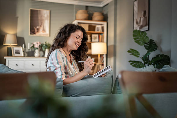 istock Young woman writing on notebook sitting on sofa at home 2216885724