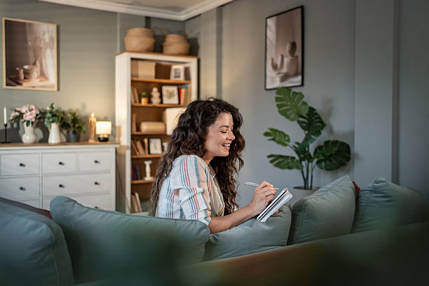 istock Young woman writing on notebook sitting on sofa at home 2216885737