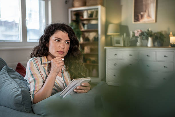 istock Thoughtful young woman making notes in notebook at home 2216885743