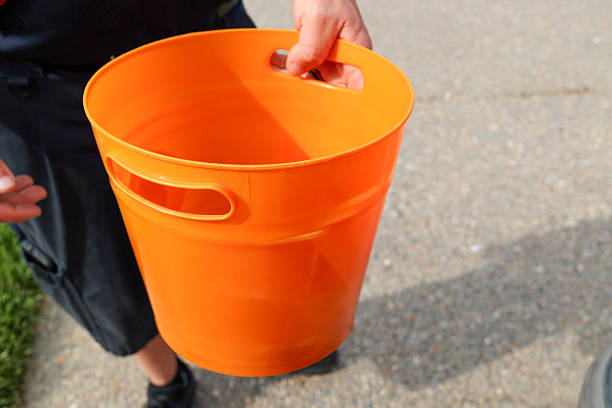 A White Man Holding A Orange Bucket For Donations