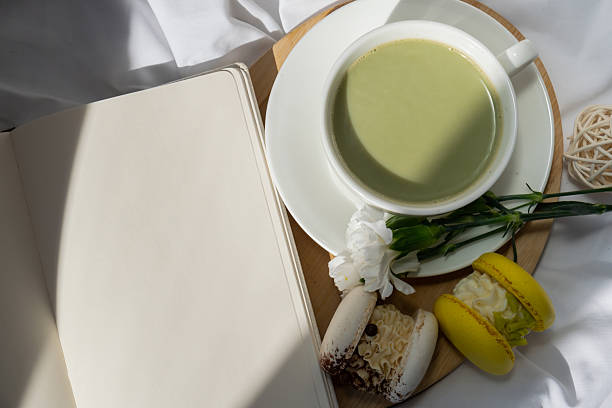 Green latte matcha sweet macaron and empty notebook self reflection journal on messy bed. Concept of holiday breakfast morning tea drink. Cozy minimalist superfood vibrant colors healthy eating. Organic caffeine-free