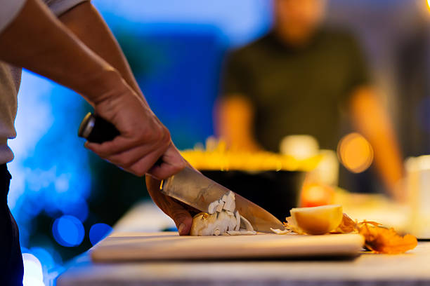 Close-up of a hand chopping onions on a cutting board while preparing ingredients in a cozy kitchen with a blurred background of soft lighting and household details.