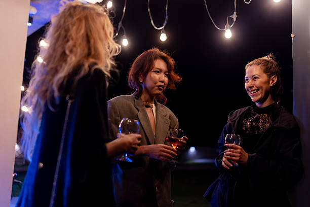 istock Three Women Enjoying a Conversation at Night Holding Glasses of Drinks Under Warm Edison String Lights 2216906963