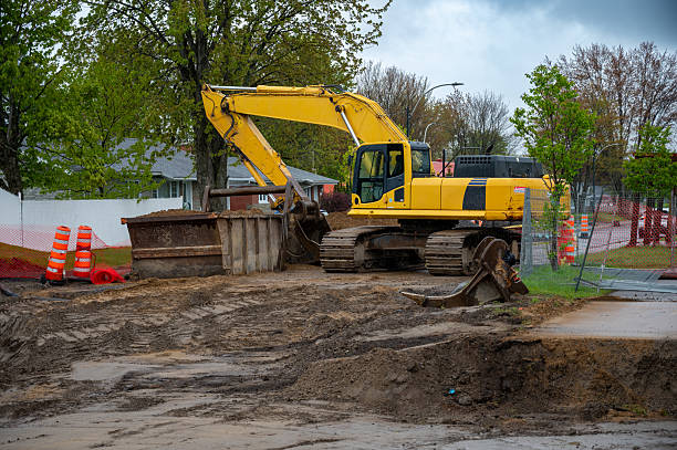 Road repair site with sand and earth foreground and an excavator in background during a cloudy day of springtime.