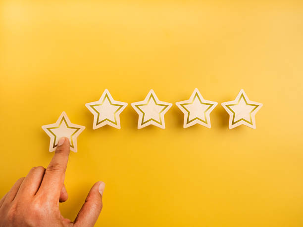 istock Five wooden stars ratings, pointing by customer hand, on yellow background. 5 points, highest level of excellence quality or satisfaction, customer evaluation ranking, business marketing concept. 2216922469