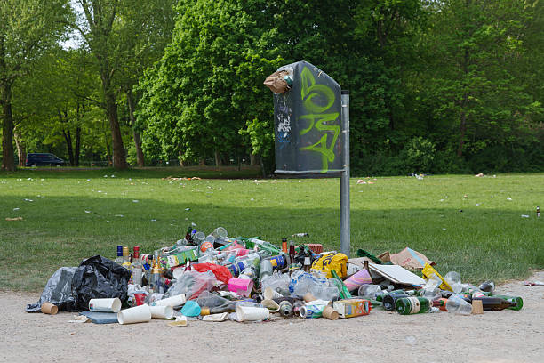 Berlin, Germany, 05.05.2025, Overflowing trash bin surrounded by a large pile of litter including bottles, cups, and plastic waste in a green public park