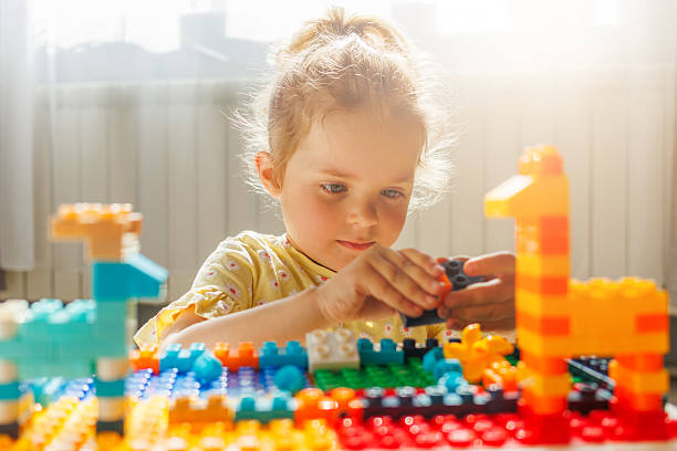 istock Young girl intently playing with colorful building blocks, creating and learning in warm sunlight. Childhood creativity and fun indoors. 2216936624