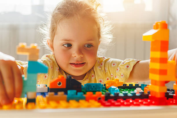 istock Young girl intently focused on building with colorful toy constructor blocks, hands busy creating in bright sunlight. Childhood play and creativity. 2216936632