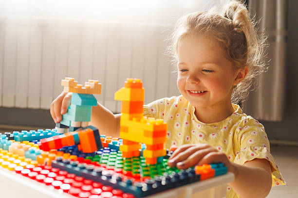 istock Smiling young girl happily builds with colorful toy constructor blocks in bright sunlight, enjoying creative play and learning through construction. 2216936638