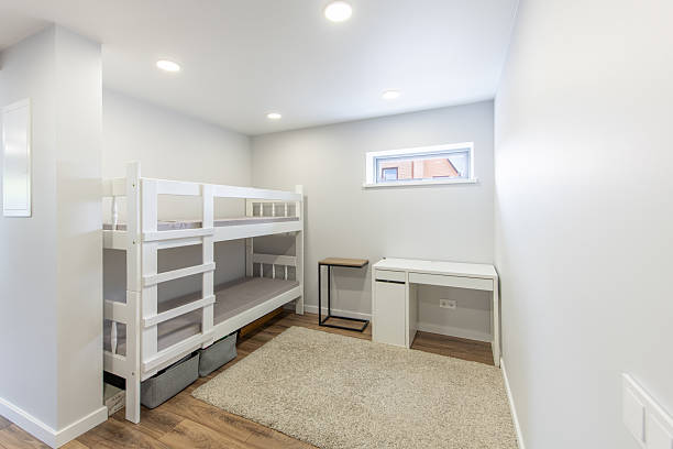 Bright and cozy minimalist bedroom featuring white bunk beds and warm hardwood flooring, illuminated by recessed lighting, radiating modern design and practicality.