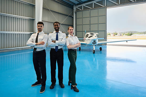 Confident student pilots posing in aircraft hangar with small plane
