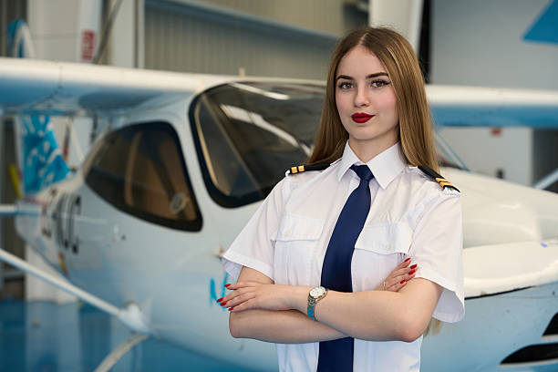 istock Confident young female pilot posing in hangar with small airplane 2216943419