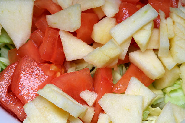A colorful mix of juicy tomatoes and crunchy apples is carefully arranged on a bed of leafy greens. The inviting atmosphere of the kitchen highlights the freshness of the ingredients.