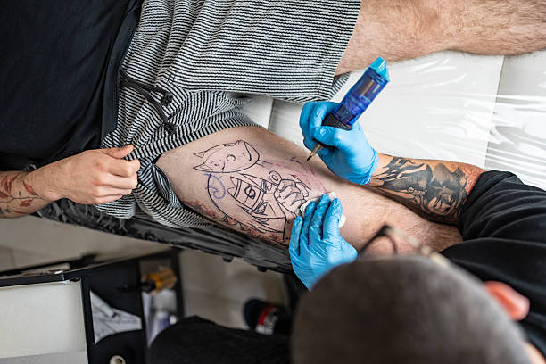 A professional tattoo artist working on a detailed tattoo design on a client's thigh. The scene showcases the artistry, precision, and passion involved in the tattooing process.