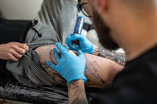 istock Tattoo Artist Applying Ink on Client's Leg in Modern Studio 2216946972