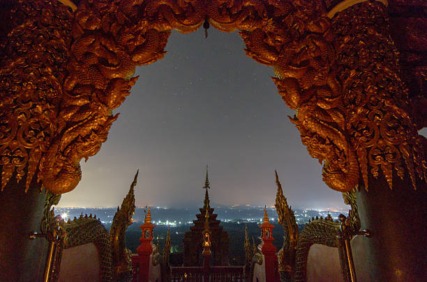 Stunning view of Lanna Buddhist temple illuminated at night, with the paths of stars gracefully curved across the starry sky. Wat Phra That Doi Phra Chan, Mae Tha District, Lampang Province