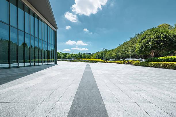 istock Empty stone pavement walkway beside a modern office building with glass facade and green garden landscape. 2216959113
