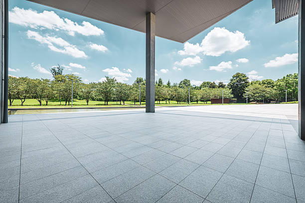 istock Empty tiled plaza floor providing a clean foreground, with a modern canopy structure above and lush green park trees under blue sky. 2216959148