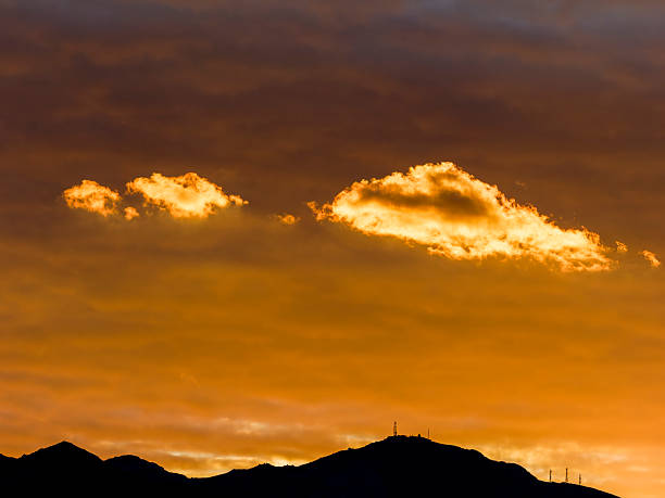 Golden clouds drift above the silhouette of mountains, capturing the serene beauty of a sunset in Marathonas, Greece.