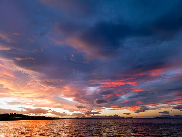The sun sets behind the horizon, casting warm hues across Chalkoutsi bay while the calm water reflects the colorful sky.