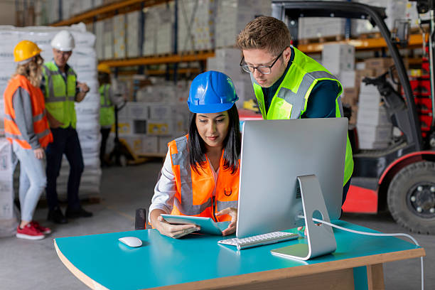 istock Young Male and Female Warehouse Workers Collaborating on a Computer with Additional Workers in the Background 2216964822