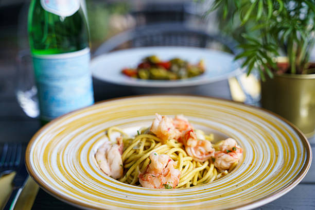 A plate of linguine pasta in a light garlic and olive oil sauce, topped with tender shrimp and garnished with fresh herbs. The dish is in a ceramic bowl on a dark wooden table.